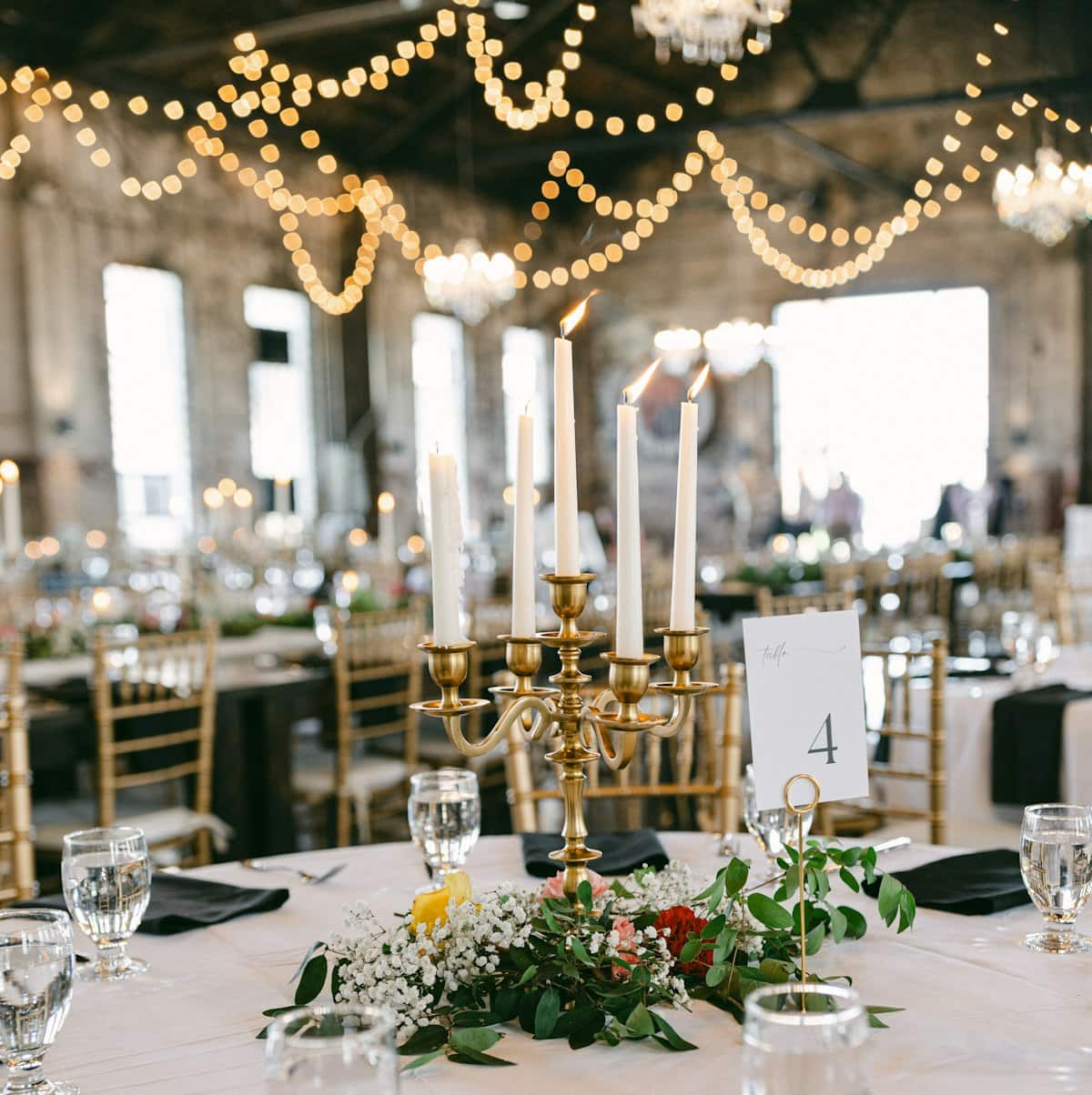 Mesa posta sob luz de lustre e varal de luzes — o clima que criamos pra cada casamento.